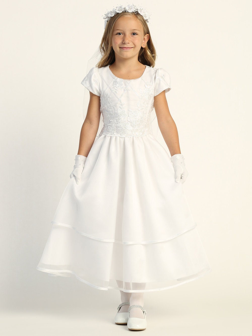 A girl wearing a stunning white First Communion Dress with embroidered tulle and sequins, featuring a soft acetate lining.